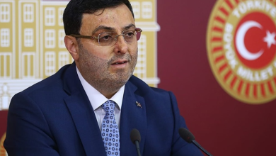 AK Parti İstanbul Milletvekili Serkan Bayram, TBMM’de düzenlenen bir basın açıklaması sırasında kürsüde konuşuyor. Üzerinde koyu renk takım elbise, beyaz gömlek ve desenli mavi bir kravat bulunuyor. Arka planda Türkiye Büyük Millet Meclisi amblemleri ve Türk bayrağı yer alıyor.