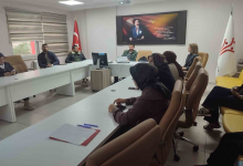 Instagram İçin Alternatif Metin: Görselin üst bölümünde, kurumsal bir toplantı odasında U şeklinde dizilmiş beyaz masaların etrafında oturan Engelli ve Yaşlı Hizmetleri personeli yer alıyor. Masalarda not dosyaları, kalemler ve bilgisayarlar bulunurken; başörtülü ve takım kıyafetli kadın ile erkek personeller dikkatle toplantıyı takip ediyor. Odanın baş tarafındaki duvarda Atatürk portresi ve vecizesi asılı duruyor; köşede Türk bayrağı ile sağ tarafta Aile ve Sosyal Hizmetler Bakanlığı'nın logosunu taşıyan beyaz bayrak görülüyor.