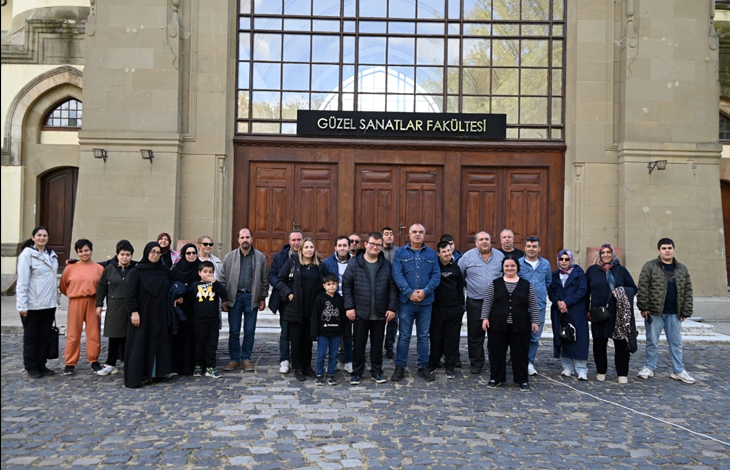 Görselin üst bölümünde, Trakya Üniversitesi Güzel Sanatlar Fakültesi'nin tarihi taş binası önündeki Arnavut kaldırımlı alanda yan yana durarak toplu hatıra fotoğrafı çektiren Çatalcalı engelli gençler, refakatçileri ve proje görevlileri yer alıyor. Geniş bir grup halinde dizilen katılımcıların arkasında, büyük ahşap çift kanatlı kapılar ve üzerinde beyaz harflerle "GÜZEL SANATLAR FAKÜLTESİ" yazan siyah tabela ile kemerli tarihi taş mimari detayları görülüyor. Günlük ve spor kıyafetleriyle kameraya gülümseyen gençler ve aileleri gezi etkinliğinin keyfini paylaşıyor.