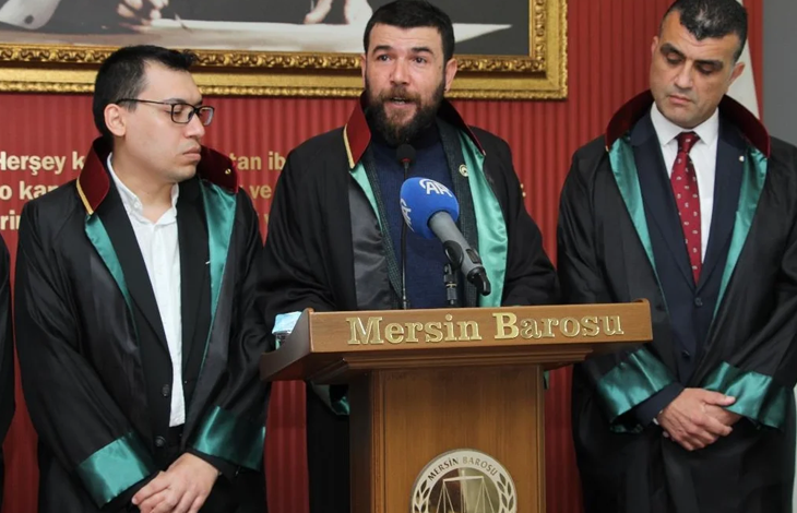 Görselin üst bölümünde, "Mersin Barosu" yazılı kürsüde avukatlık cübbesi giymiş bir avukat basın açıklaması yaparken, yanında destek amacıyla bulunan diğer iki avukatla birlikte yer almaktadır. Ortada sakallı ve cübbeli olarak konuşmayı yapan avukatın sağında gözlüklü, solunda ise koyu takım elbiseli ve kırmızı kravatlı meslektaşları ciddiyetle dinlemektedir. Arka planda kırmızı tonlarda pano ve üzerinde adalet temalı görseller ile yazılar bulunmaktadır.
