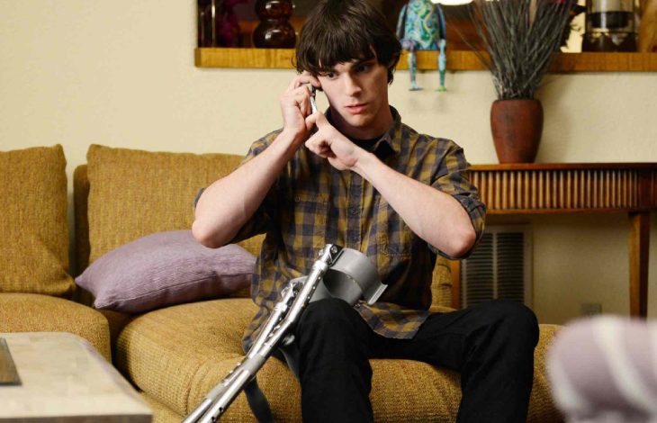 Engelli oyuncu RJ Mitte, sarı koltukta otururken bir eliyle telefonla konuşup diğer eliyle koltuk değneğini tutmaktadır.