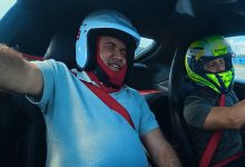 Görselde, otomobilin içinde kask takmış iki kişi görülüyor; öndeki kişi Levent Karadöl heyecanlı bir ifadeyle gözlerini kapatırken, Felipe Massa direksiyonda aracı kullanıyor.