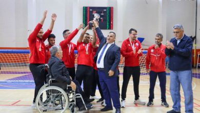 Sporcuların kırmızı formalarıyla kupayı kaldırarak sevinçlerini paylaştığı salonda, takım arkadaşları ve yöneticiler büyük bir coşkuyla şampiyonluğu kutlarken çevredekiler onları alkışlayarak tebrik etmektedir.