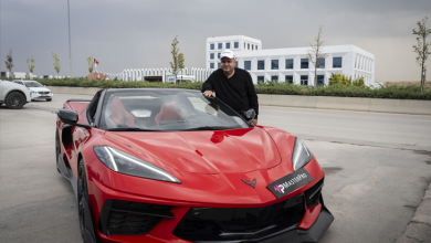 Görselin üst bölümünde, açık alanda park edilmiş parlak kırmızı renkli spor bir otomobilin hemen yanında durarak poz veren görme engelli Levent Karadöl yer almaktadır. Siyah üst giyen ve beyaz şapka takan Karadöl, elini spor arabanın ön cam çerçevesine dayamış vaziyette kameraya bakmaktadır. Arka planda modern beyaz binalar, yol kenarı ve bulutlu gri bir gökyüzü görülmektedir.