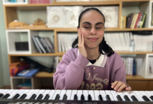 Instagram İçin Alternatif Metin: Görselin üst bölümünde, bir müzik odasında klavyenin (synthesizer) başında oturarak hafifçe gülümseyen görme engelli müzisyen Duygu Murcak yer alıyor. Üzerinde lila renkli kapüşonlu veya sweatshirt tarzı bir üst giysi bulunan genç kadın, sağ elini yanağına dayamış vaziyette poz verirken sol eliyle klavyenin tuşlarına dokunuyor. Arkasındaki ahşap raflı kitaplıkta düzenli bir şekilde dizilmiş dosyalar, kitaplar ve çeşitli eşyalar dikkat çekiyor.