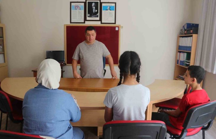 Görselde, rehber öğretmen Hasan Akyürek sınıfta öğrencilerin karşısında masa başında durarak ders anlatırken, öğrenciler dikkatle onu dinlemektedir.