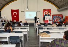 Görselde, Türk bayrakları ve Atatürk posteriyle süslenmiş bir salonda, katılımcıların masa başında oturarak bir konuşmacının sunumunu dinlediği spor ve yaşlılık temalı bir kongre veya eğitim etkinliği görülmektedir.