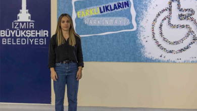 Görselin üst bölümünde, kapalı bir alanda, üzerinde "İZMİR BÜYÜKŞEHİR BELEDİYESİ" yazısı ve "FARKLILIKLARIN FARKINDAYIZ" afişi ile tekerlekli sandalye simgesi bulunan bir duvarın önünde ayakta durarak doğrudan kameraya bakan işitme engelli Sahra Nur Akyıl yer almaktadır. Siyah uzun kollu gömlek ve mavi kot pantolon giymiş olan Akyıl, hafifçe gülümseyerek poz vermektedir.