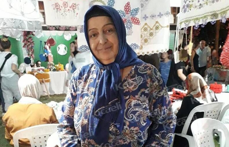 Görselin üst bölümünde, el emeği ürünlerin sergilendiği bir kermes veya pazar yerinde tezgâhının önünde durarak hafifçe gülümseyen engelli pazarcı Durdu Bayrak yer alıyor. Mavi tonlarında desenli bir elbise giyen ve lacivert başörtüsü takmış olan kadının başörtüsünün yakasında okuma gözlüğü asılı duruyor. Çevresinde ve başının üzerinde el işi danteller, işlemeli örtüler ve örgüler sergilenirken; arka planda beyaz plastik sandalyeler, stantları gezen vatandaşlar ve pazar alanının kalabalığı görülüyor.