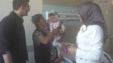 Görselde, bir hastane odasında yatağın yanında duran aile bireyleri ve başörtülü bir yetkili yer almaktadır. Annesinin kucağında tuttuğu, başı sargılı olan küçük bir çocuk ve sol tarafta duran bir erkek aile bireyi ile sağ taraftaki ziyaretçi yetkili, çocukla ilgilenirken görülmektedir.