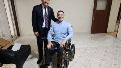 Görselde, iç mekanda akülü tekerlekli sandalyede oturan engelli bir vatandaş ile yanında ayakta durarak poz veren takım elbiseli bir yetkili yer almaktadır.