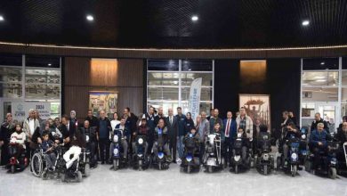 Akülü tekerlekli sandalye kullanan engelliler ile yetkililer beraber törende poz veriyorlar.
