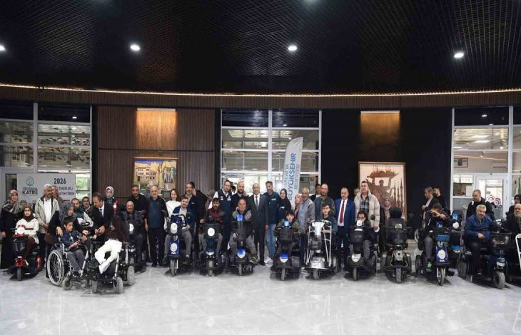 Akülü tekerlekli sandalye kullanan engelliler ile yetkililer beraber törende poz veriyorlar.