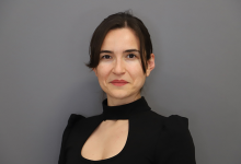 Görselde, sade gri bir arka plan önünde profesyonel bir portre çekimi yapılmış. Elif Türel, koyu renkli, yüksek yakalı ve göğüs kısmında küçük bir kesim detayı bulunan şık bir üst giyiyor. Saçları düzgünce geriye taranmış ve yüz hatlarını net şekilde ortaya çıkaran yumuşak bir ışık kullanılmış. Duruşu dik, ifadesi kendinden emin ve akademik bir profesyonelliği yansıtıyor.