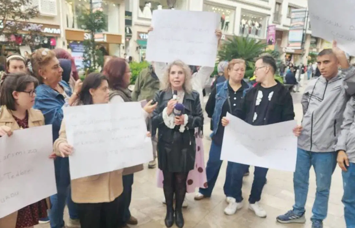 Görselin üst bölümünde, şehir merkezindeki kalabalık bir meydanda toplanarak basın açıklaması ve protesto gerçekleştiren engelli bireyler ile aileleri yer alıyor. Grubun ortasında siyah deri ceketli ve etekli bir kadın elindeki mikrofonla açıklama yaparken, arkasındaki ve yanındaki katılımcılar ellerinde beyaz protesto dövizleri taşıyor. Ön planda ve yanlarda duran gençler ile aileleri tepkilerini dile getirirken; arka planda yayalar, cadde üzerindeki mağazalar ve şehir binaları görülüyor.