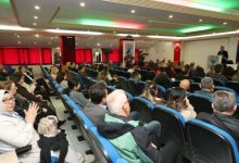 Katılımcılar seyirci koltuğunda kürsüde konuşan kadını dinliyor.