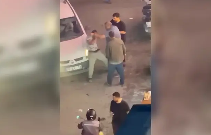 Görselin üst bölümünde, akşam saatlerinde sokak lambaları altında gerçekleşen darp anına ait güvenlik kamerası veya cep telefonu kaydı perspektifi yer alıyor. Beyaz bir hafif ticari aracın önünde duran açık renk kıyafetli engelli seyyar satıcıya doğru yönelen ve onu tartaklayan şüpheli ile araya girmeye çalışan çevredeki kişiler görülüyor. Ön planda kasklı bir motosiklet sürücüsü ve yoldan geçen diğer vatandaşlar kadrajda dikkat çekiyor.