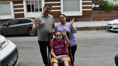 Görselin üst bölümünde, sokakta özel destekli çocuk tekerlekli sandalyesinde oturan serebral palsili küçük kız çocuğu Yağmur ve hemen arkasında duran anne ile babası yer alıyor. Sandalyede oturan Yağmur, fuşya renkli tişörtü ve bej şortuyla hafifçe gülümseyerek sol elini havaya kaldırıp selam veriyor. Arkasındaki gri polo yaka tişörtlü babası ile açık mor tişörtlü annesi de neşeyle birer ellerini kaldırarak kameraya el sallıyor. Arka planda modern bir apartman binası, sokakta park halinde duran gri ve beyaz renkli otomobiller görülüyor.