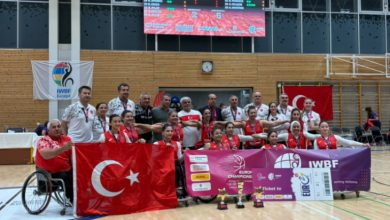Türkiye Tekerlekli Sandalye Kadın Basketbol Takımı, spor salonunda Türk bayrakları ve Avrupa Şampiyonası pankartları eşliğinde önlerinde kupa ve madalyalarıyla birlikte gururla poz veriyor.