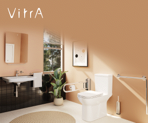 Reklam görselinde, modern ve sade bir banyo bulunuyor. Açık bej tonlarında duvarlar, büyük bir pencere ve ferah bir aydınlık ortam dikkat çekiyor. Solda beyaz bir klozet yer alıyor; yanında engelli bireylerin güvenli şekilde oturup kalkmasını sağlayan metal destek kolu bulunuyor. Klozetin yanında küçük bir yeşil bitki yerleştirilmiş. Sağ tarafta duvara monte edilmiş beyaz bir lavabo ve üstünde dikdörtgen bir ayna var. Lavabonun yanında havlu askısı bulunuyor. Zeminde açık renkli bir banyo paspası yer alıyor. Görselin üzerinde “VitrA – Özel ihtiyaçlar, özel çözümler” yazısı bulunuyor. Bu ifade, VitrA’nın engelli bireylerin bağımsız yaşamını destekleyen erişilebilir banyo çözümleri sunduğunu vurguluyor.