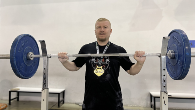Görselde, spor salonunda halter barını kaldıran veya tutan, boynunda madalya takılı olan bir sporcu yer almaktadır.