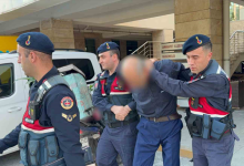 Instagram İçin Alternatif Metin: Görselin üst bölümünde, adliye binası önünde jandarma ekipleri tarafından kolları tutularak sevk edilen bir şüpheli yer alıyor. Mavi gömlek ve koyu renk pantolon giymiş olan şüphelinin yüzü mozaiklenerek gizlenmiş olup başı öne eğik vaziyettedir. Şüphelinin her iki yanında ve önünde, lacivert üniformalı, mavi bereli ve hücum yelekli jandarma personeli bulunuyor. Arka planda beyaz bir jandarma aracı, adliye binasının sütunları ile girişteki "CUMHURİYET BAŞSAVCILIĞI / MAHKEMELER" tabelası görülüyor.